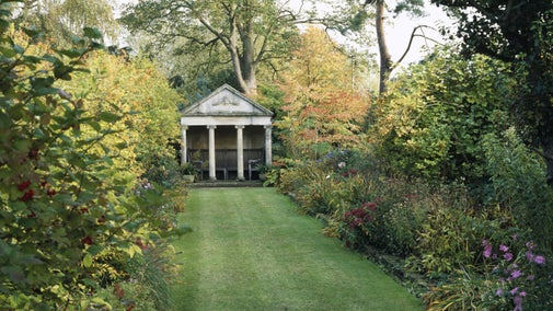 A stretch of lawn leading up to The Temple at The Courts Garden with autumnal borders and trees either side in Wiltshire.